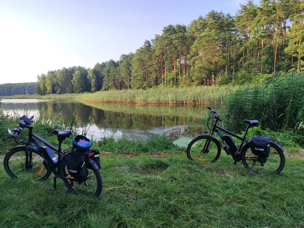 Planowanie wyprawy na rowerze elektrycznym – dwa rowery elektryczne z sakwami podczas postoju nad jeziorem przy lesie