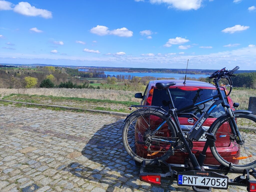 Rower elektryczny przewożony na platformie rowerowej Spinder TX2 LED na haku samochodu z widokiem na jezioro w tle