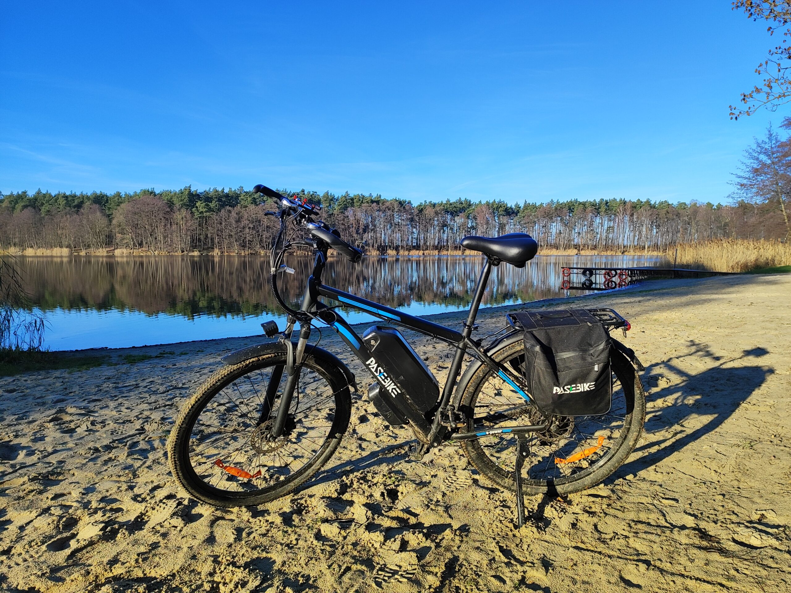 Pasebike C29 Pro rower elektryczny na plaży nad jeziorem z sakwami i baterią na ramie