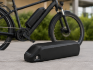 Zamienna bateria do roweru elektrycznego leżąca obok czarnego e-bike’a.