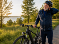 Starszy rowerzysta w kasku stoi przy rowerze elektrycznym i trzyma się za kark – ból szyi po jeździe na rowerze